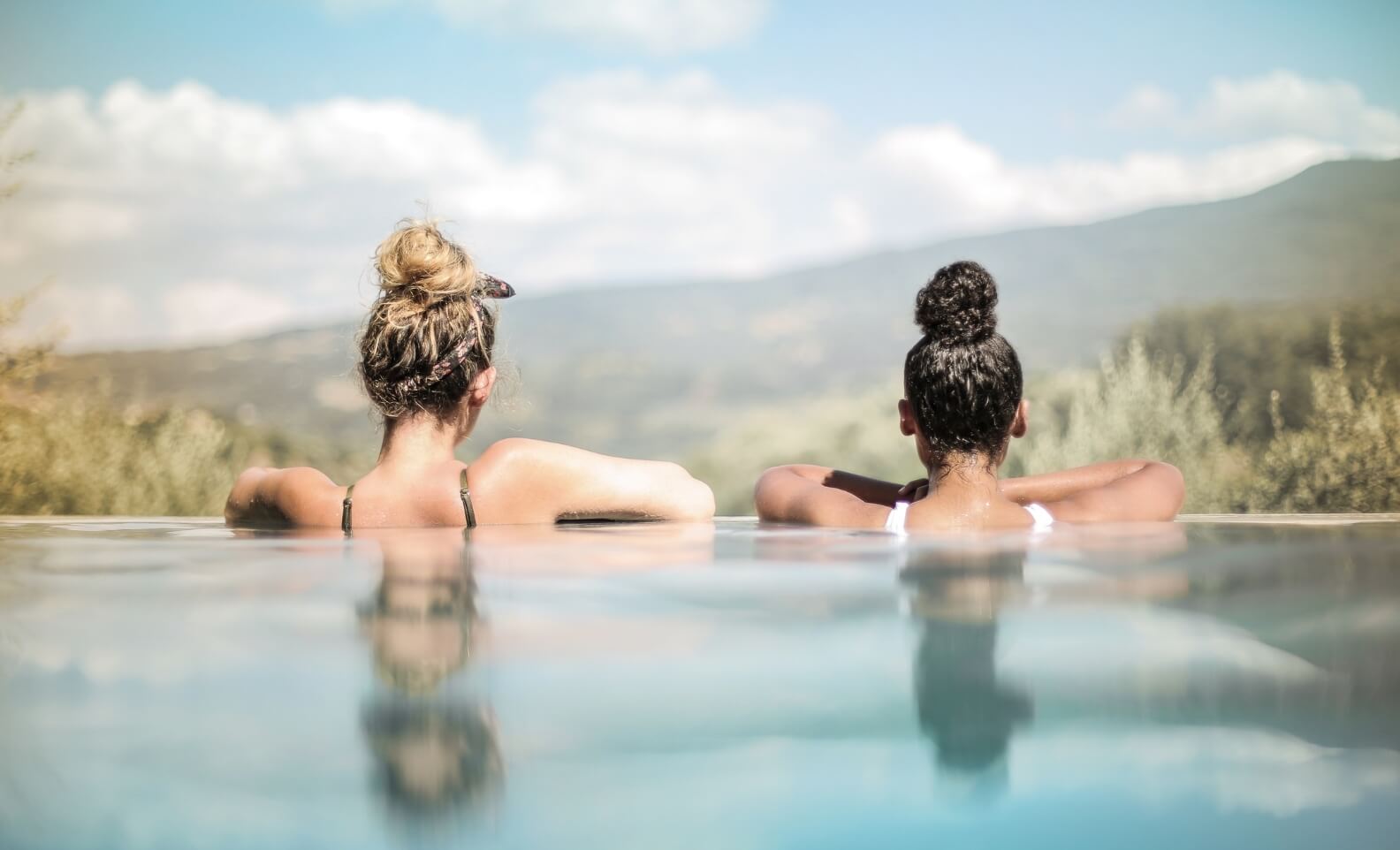 Two Selfless women enjoying a relaxing moment in a pool with a scenic landscape view in the background