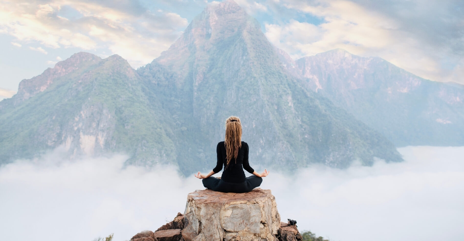 A woman meditating overlooking a serene mountain landscape showcasing abundance.