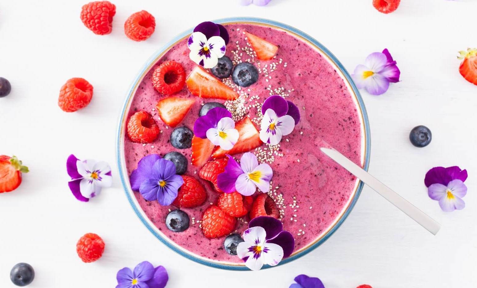 Aesthetic smoothie bowl adorned with colorful edible flowers and mixed berries