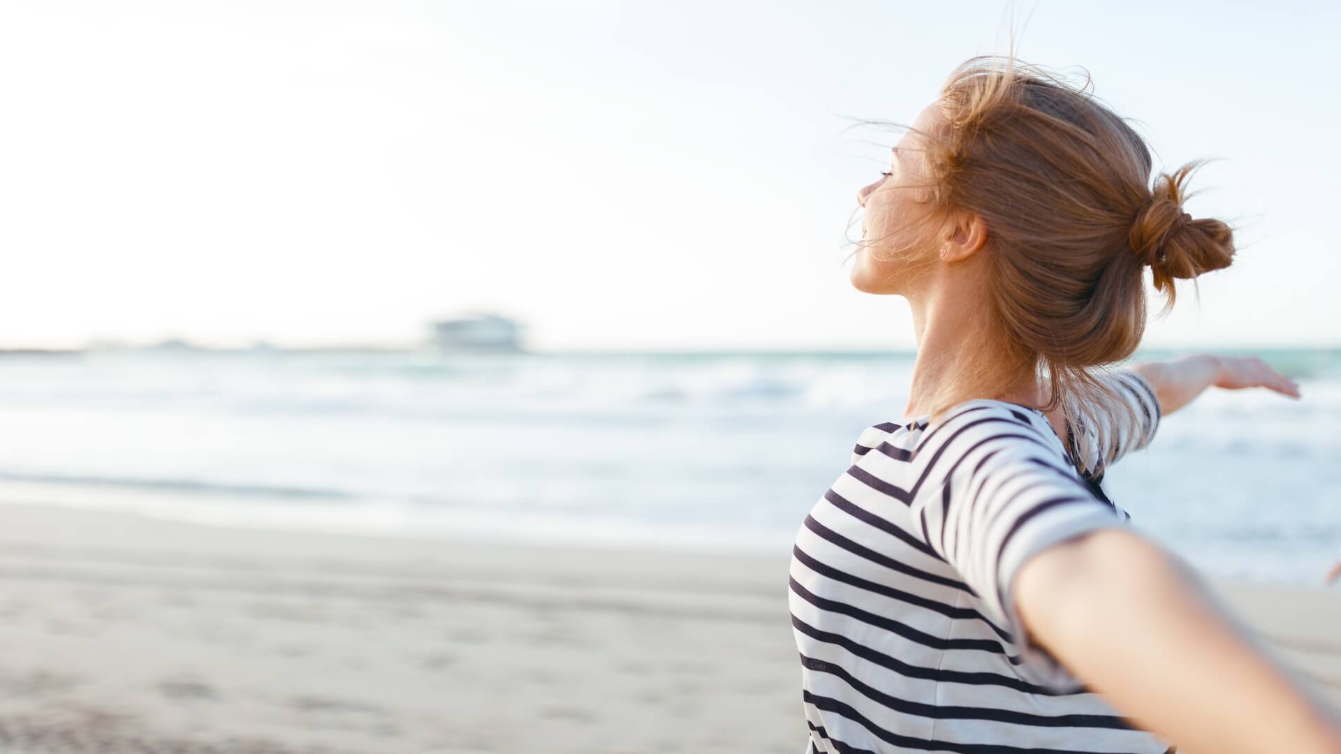 A woman at the beach with her arms spread out wide, embodying the abundance mindset.