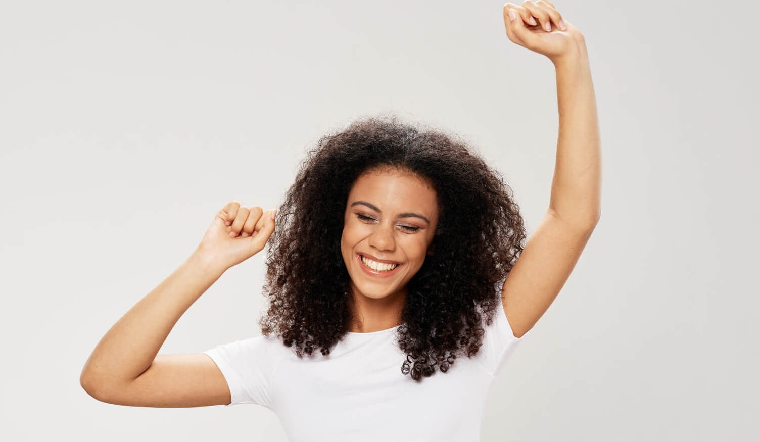A joyful woman smiling with her arms raised in the air, signifying the freedom and happiness from her authenticity in mental wellness.