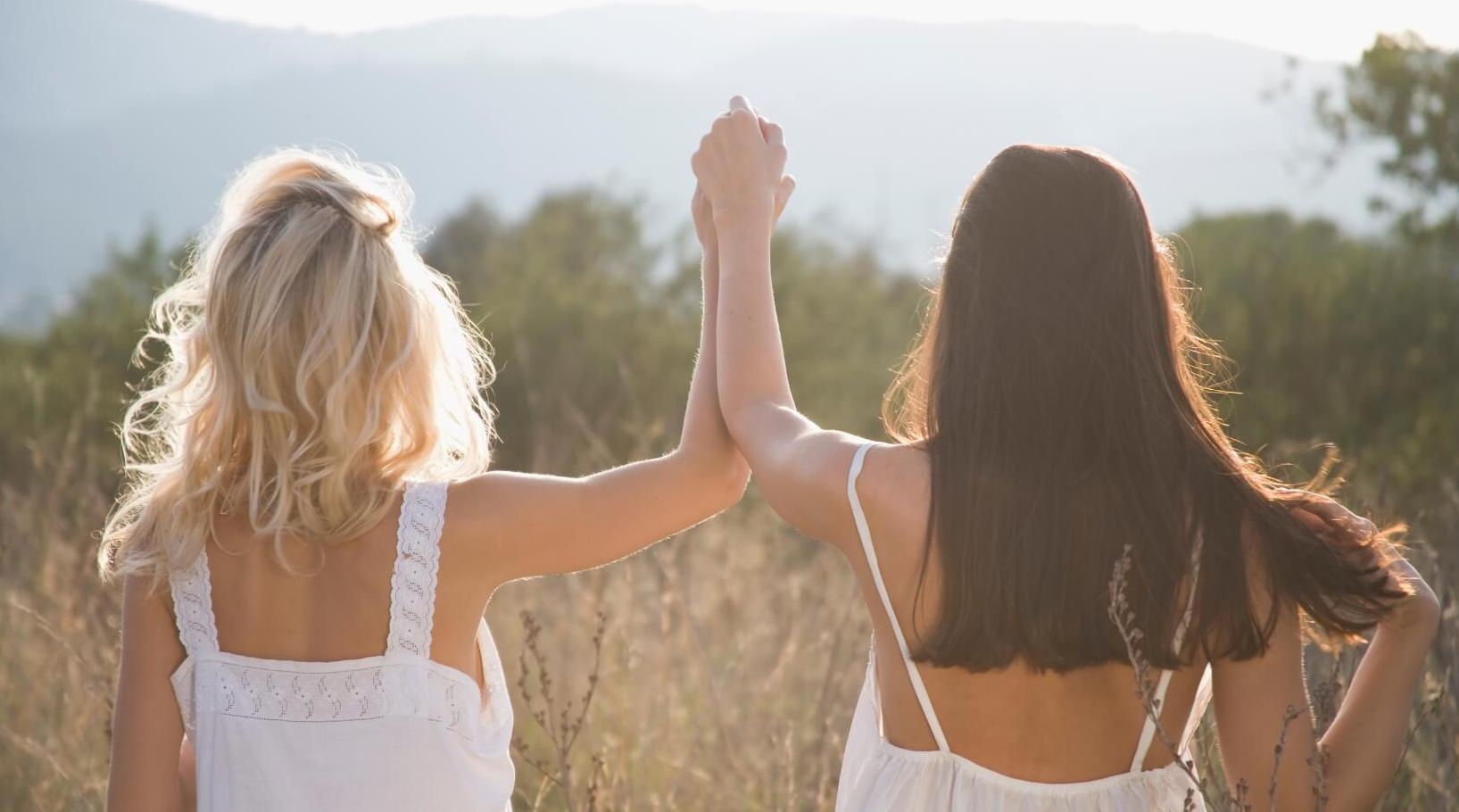 Two women in a meadow holding hands, symbolizing strong relationships through mindfulness