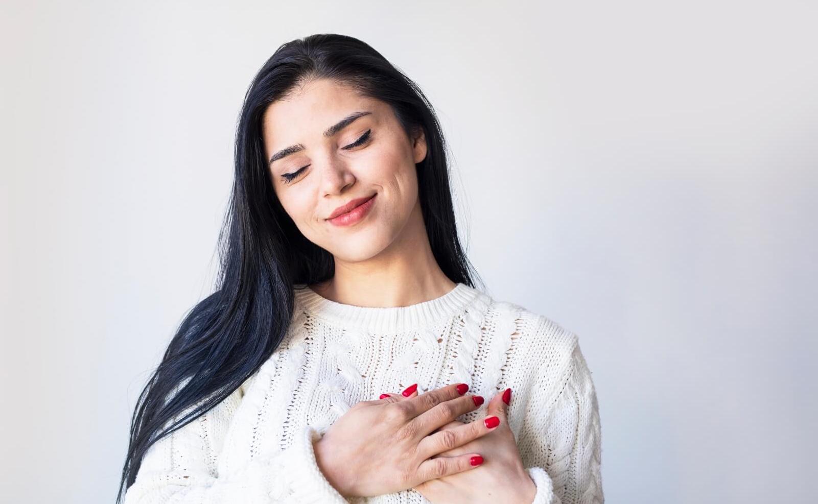 A woman smiling with her hands on her chest, embodying the concept of self-compassion.
