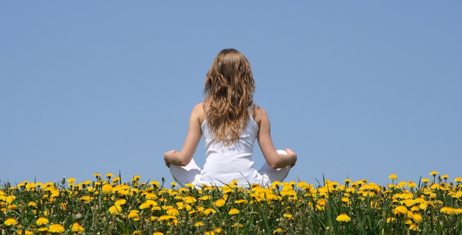 A woman practicing mindfulness while sitting peacefully in a sunflower field, illustrating the benefits of mindfulness for mental well-being.